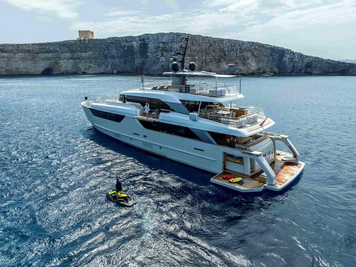 A sleek yacht cruises in clear blue waters near a rocky coastline. aboard UNIQUE S Yacht for Sale
