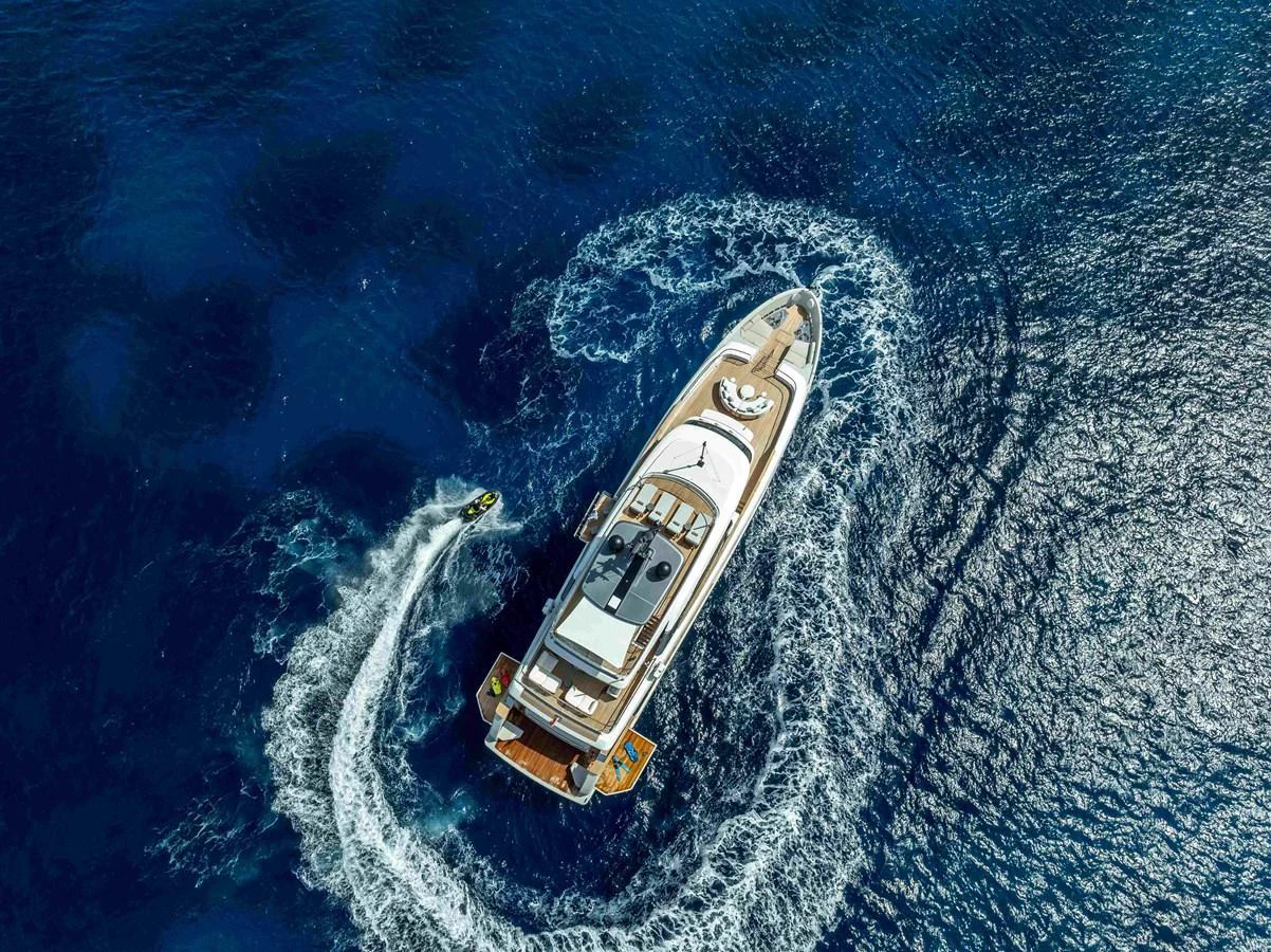 An aerial view of a luxurious yacht cruising through deep blue waters, accompanied by a jet ski. aboard UNIQUE S Yacht for Sale