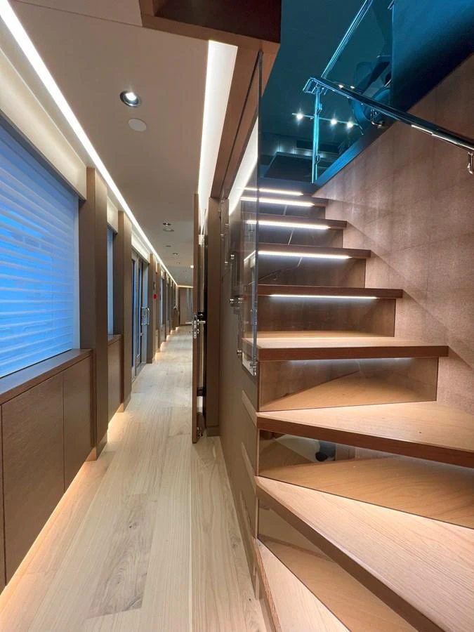 A modern yacht interior featuring a sleek wooden staircase and a well-lit hallway. aboard WESTPORT 117 / 35M Yacht for Sale