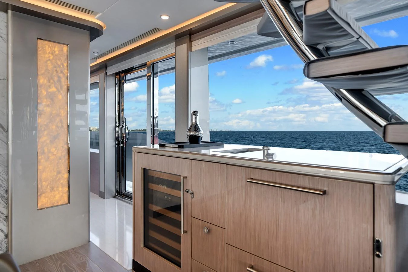 A modern yacht interior featuring a kitchenette with a wine cooler and a view of the ocean through large windows. aboard OCEAN ALEXANDER 37L Yacht for Sale
