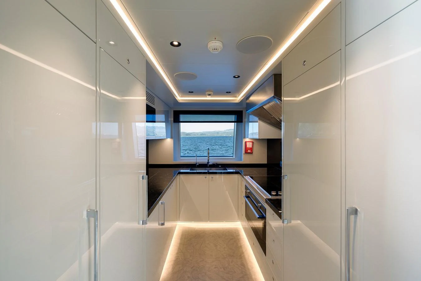 A sleek and modern galley with high-gloss cabinetry and a large window offering a view of the sea. aboard SPRITZ 116 Yacht for Sale