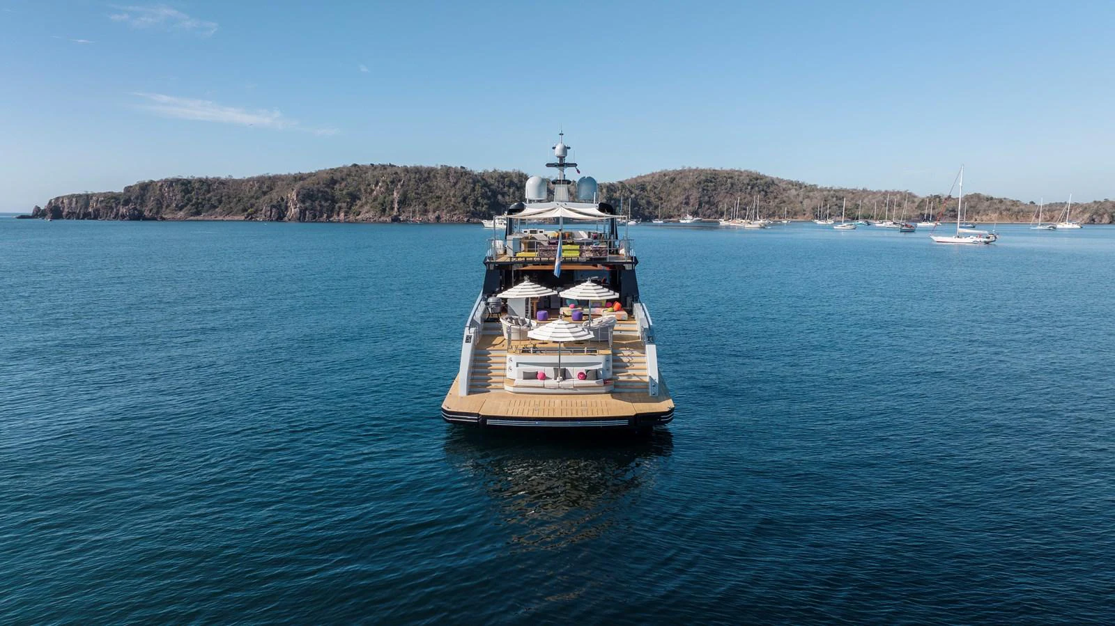 A luxurious yacht is anchored in a serene bay, showcasing its spacious aft deck with elegant seating and sunbathing areas. aboard SPRITZ 116 Yacht for Sale