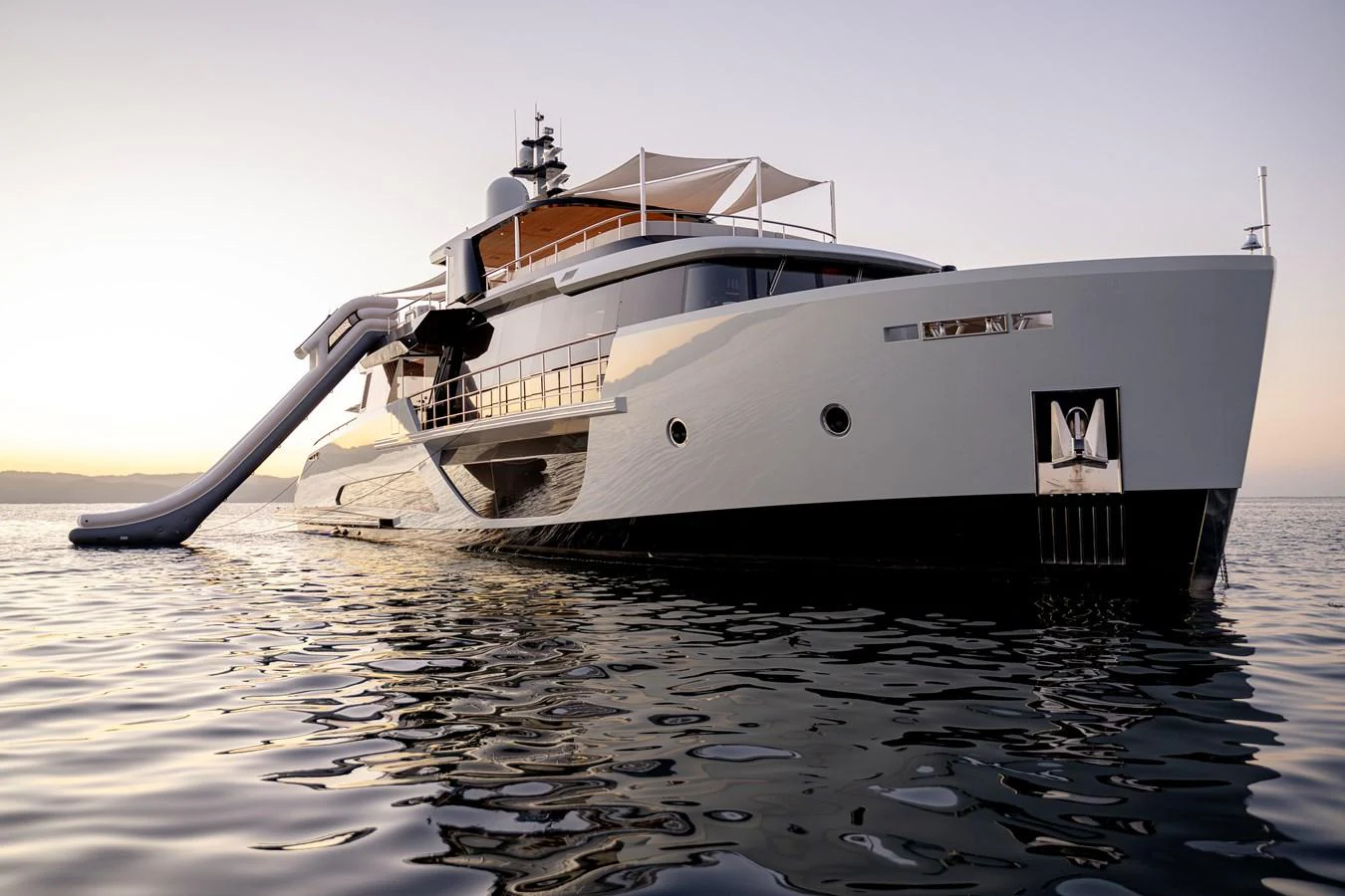 A sleek and modern yacht with a waterslide, cruising on calm waters at sunset. aboard H2O - SPRITZ 116 Yacht for Sale
