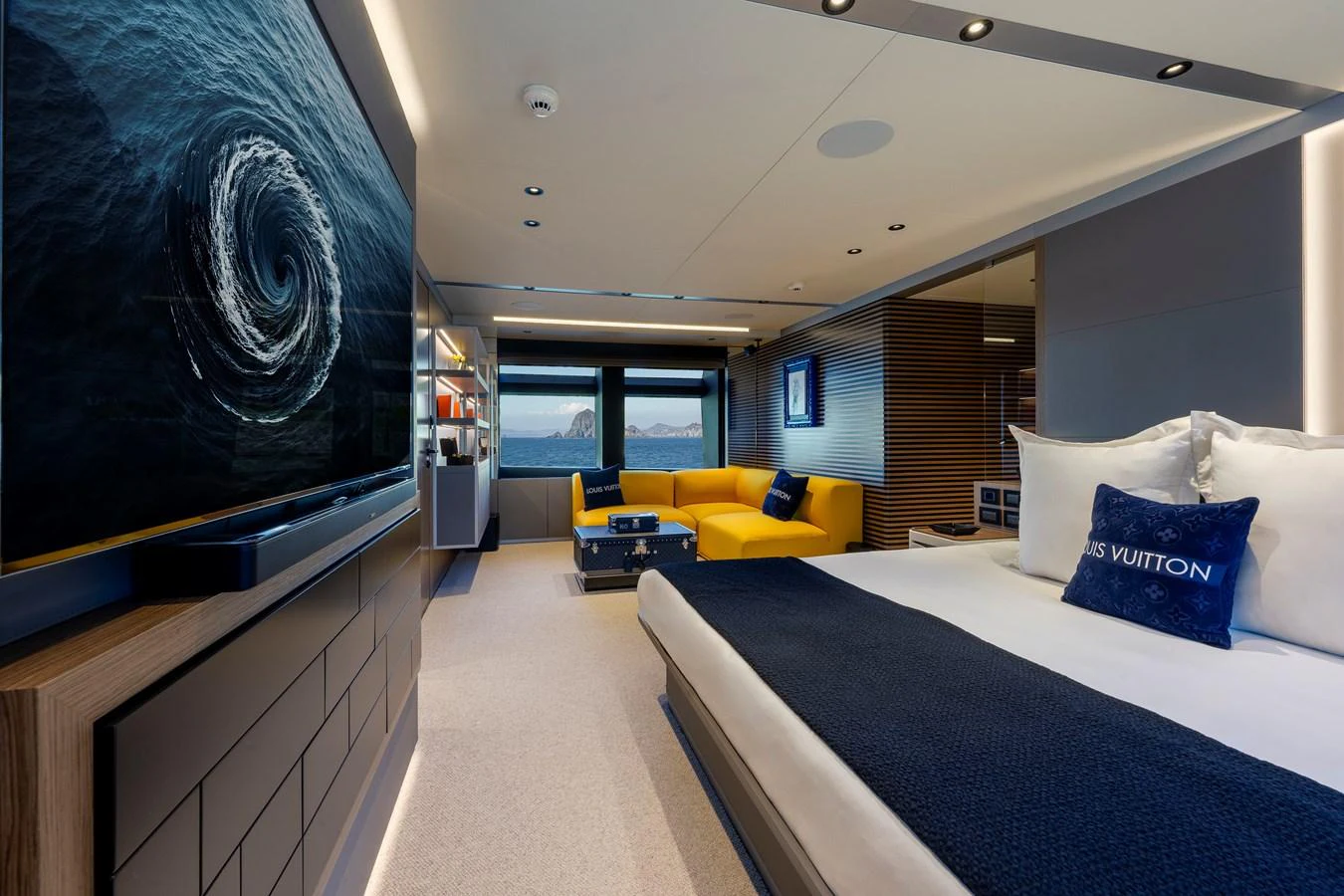 A luxurious stateroom featuring a large bed, a vibrant yellow sofa, and a flat-screen TV with a mesmerizing oceanic display. aboard H2O - SPRITZ 116 Yacht for Sale