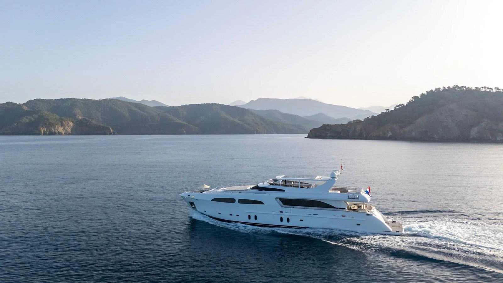 A luxurious yacht cruises through serene waters with a picturesque mountainous backdrop. aboard JAFE TICA Yacht for Sale