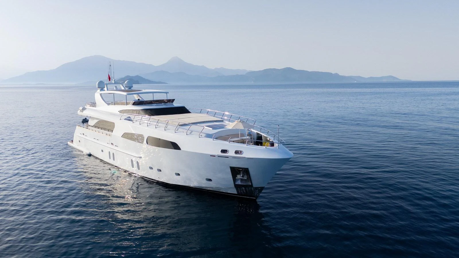 A sleek and modern yacht glides gracefully on calm waters with a stunning mountainous backdrop. aboard JAFE TICA Yacht for Sale