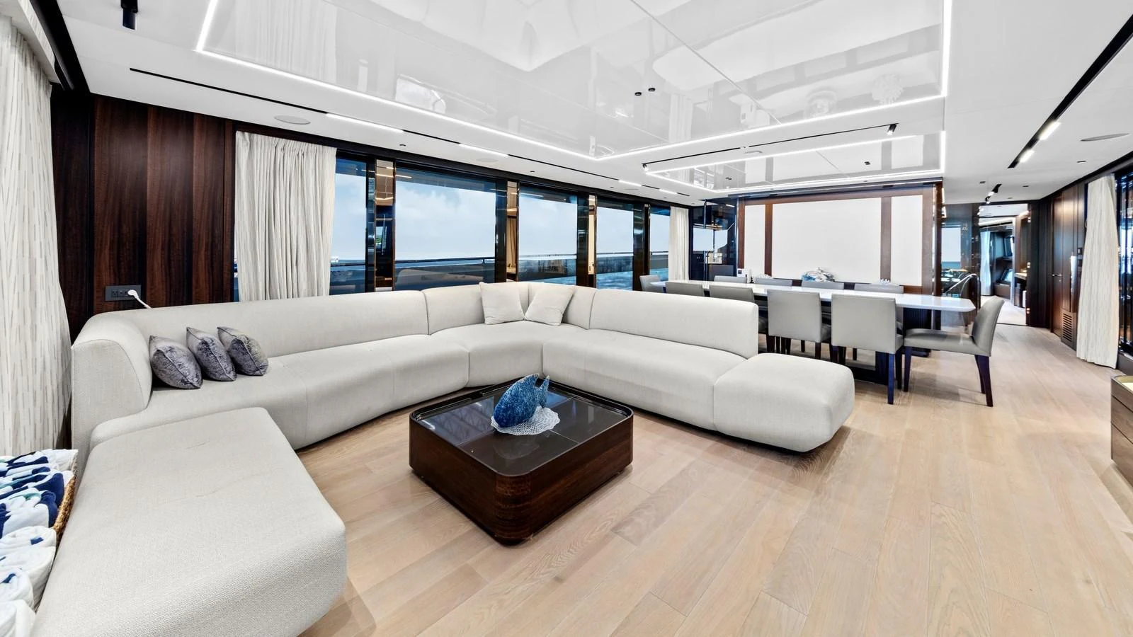 The spacious salon features a large, elegant L-shaped sofa and a modern dining area with panoramic windows. aboard CONTESSA Yacht for Sale