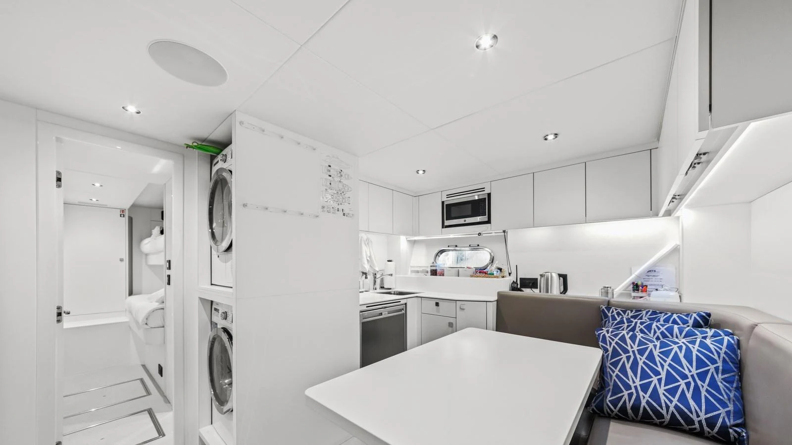The modern galley features sleek white cabinetry and a cozy dining area with vibrant blue accent pillows. aboard CONTESSA Yacht for Sale