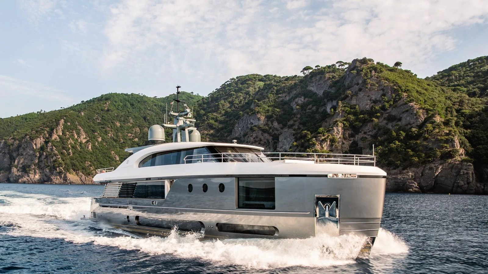 A sleek and modern yacht cruises through clear waters with a scenic mountainous backdrop. aboard ARIA Yacht for Sale