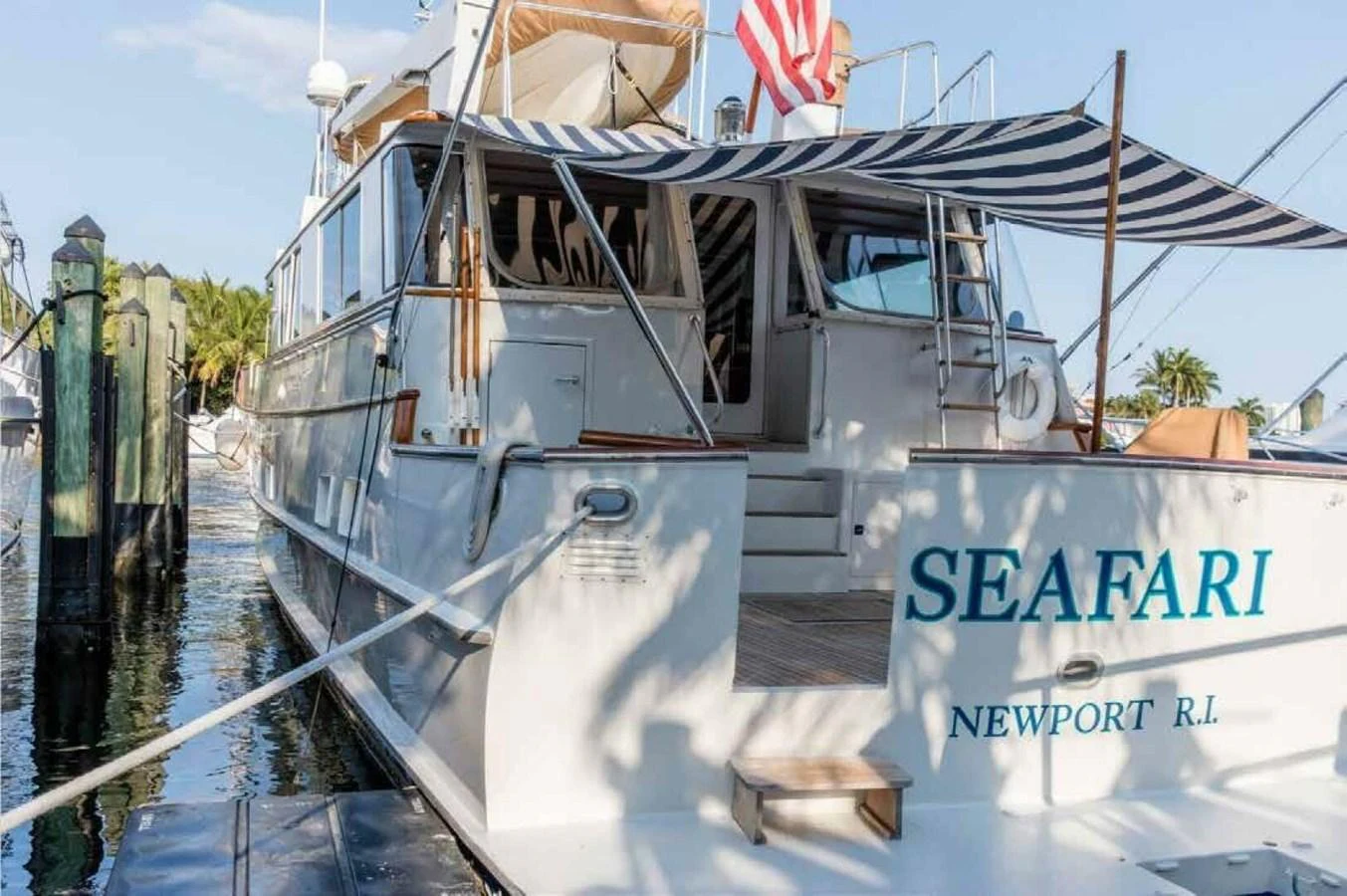 The yacht's aft deck features a striped canopy and a welcoming entrance, docked in a serene marina. aboard SEAFARI Yacht for Sale