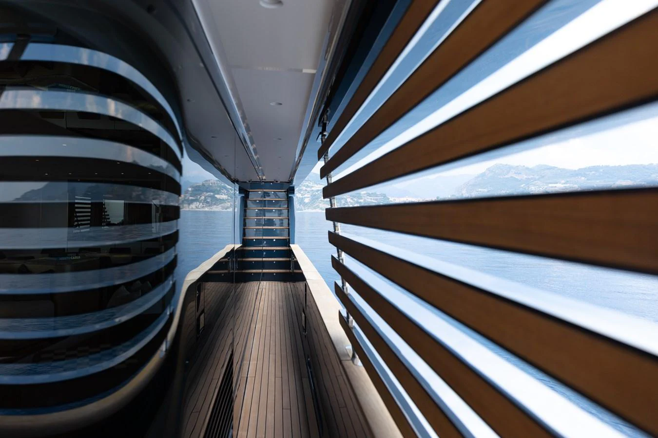 A sleek exterior walkway with modern design elements and a stunning view of the water and mountains. aboard PALMAX Yacht for Sale