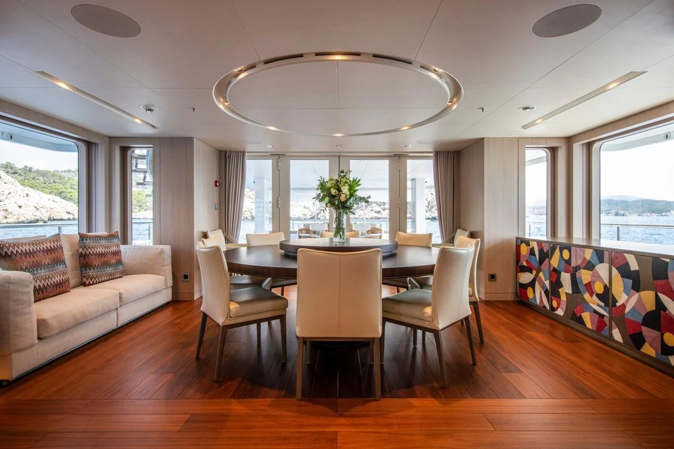 The yacht's dining area features a round table with elegant seating, surrounded by large windows offering scenic views. aboard PROMISE Yacht for Sale
