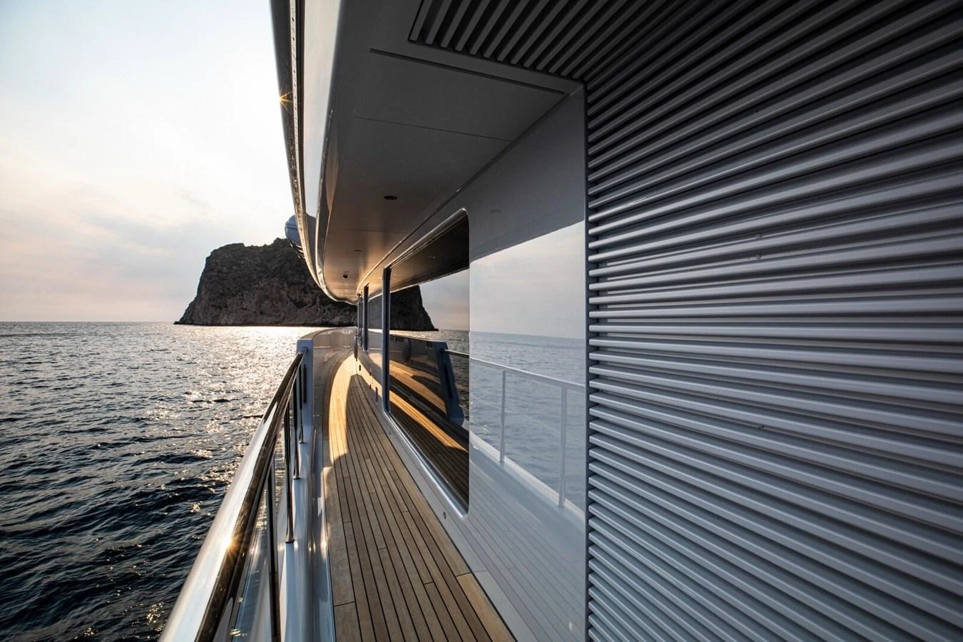 The sleek side deck of the yacht offers a stunning view of the sea and distant cliffs. aboard PROMISE Yacht for Sale