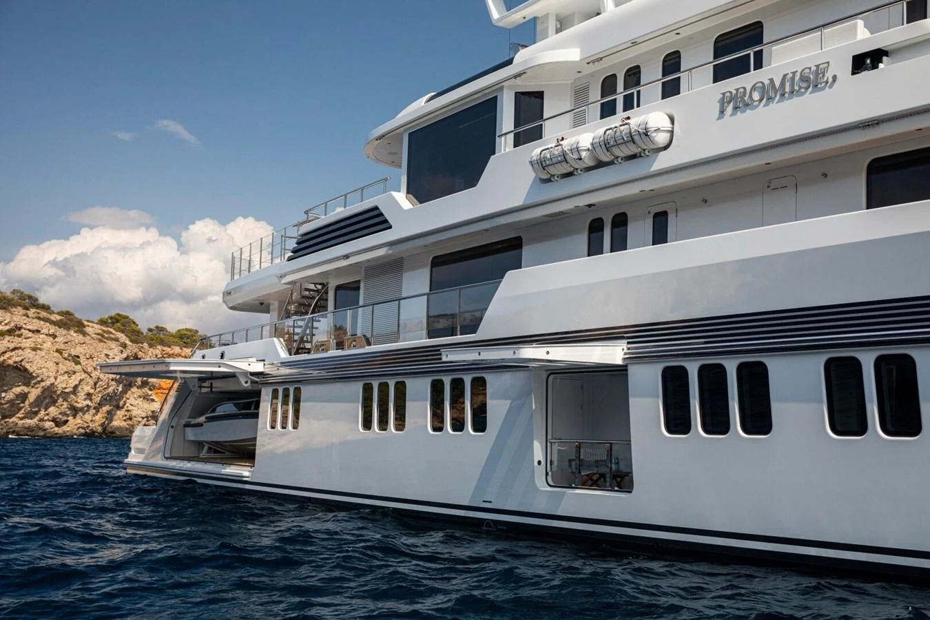 A luxurious yacht is anchored near a rocky coastline, showcasing its sleek design and multiple decks. aboard PROMISE Yacht for Sale