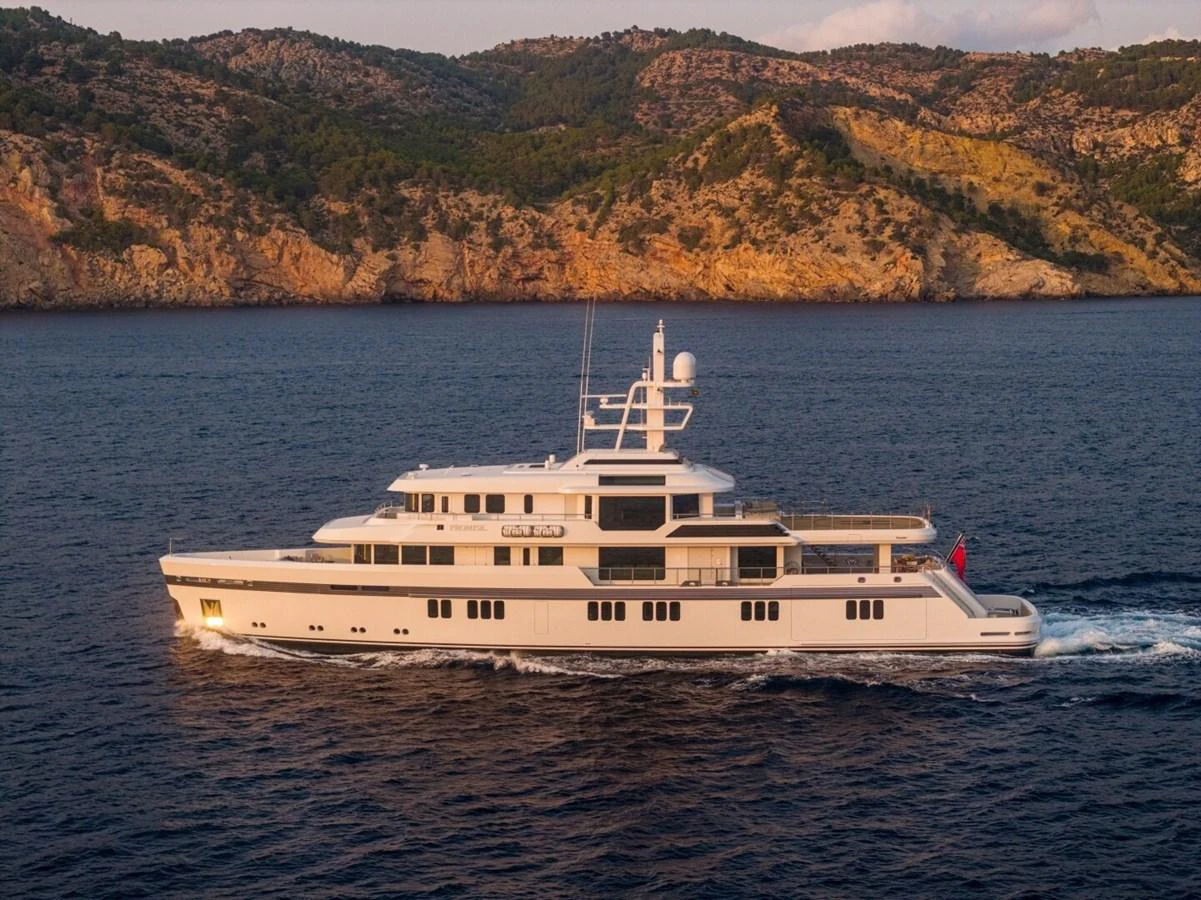A sleek yacht cruises along a serene coastline with picturesque hills in the background. aboard PROMISE Yacht for Sale