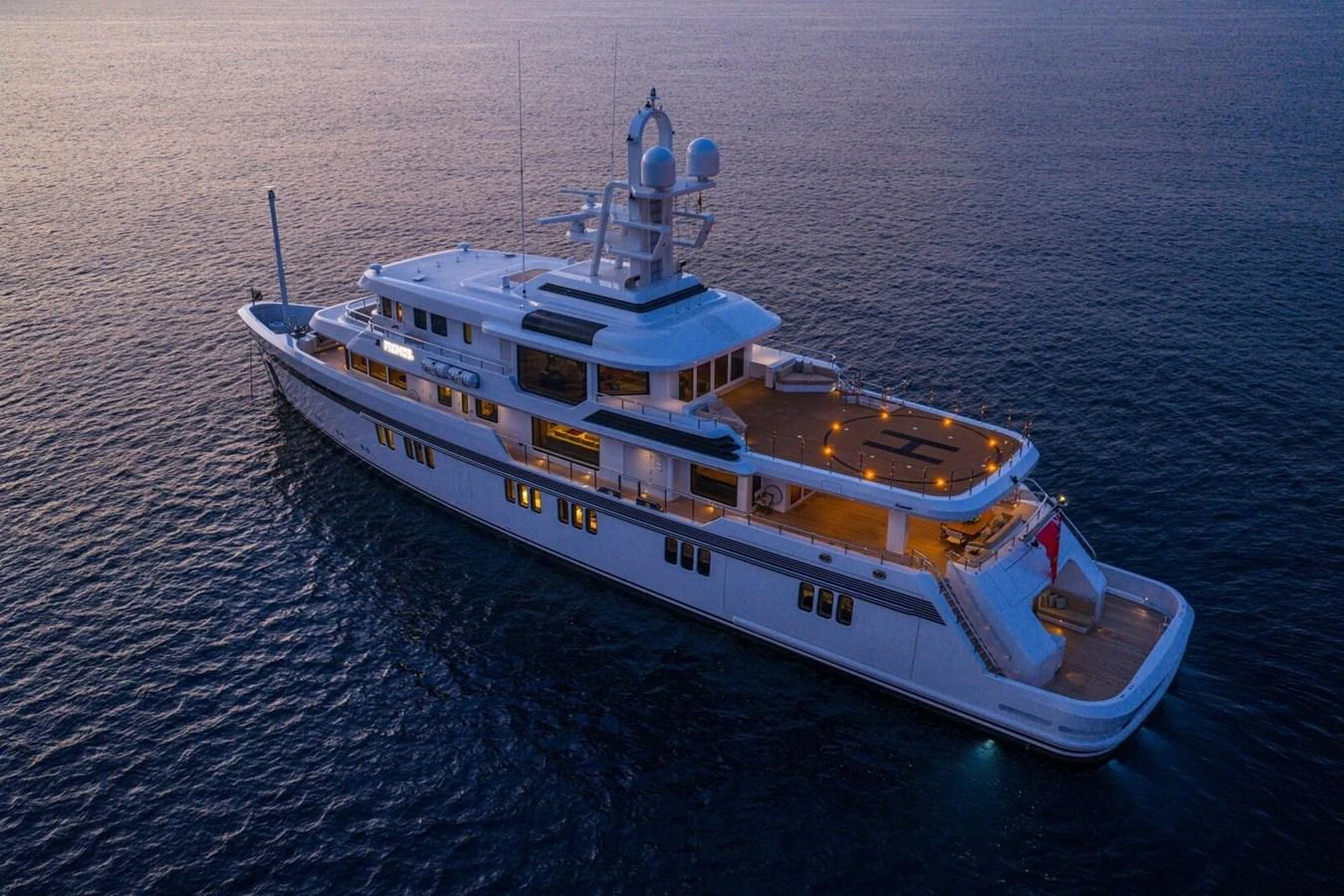 A luxurious yacht is anchored in calm waters during twilight, showcasing its elegant design and illuminated decks. aboard PROMISE Yacht for Sale