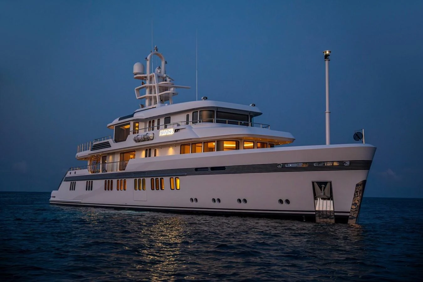 A luxurious yacht is illuminated against the twilight sky, showcasing its elegant design and spacious decks. aboard PROMISE Yacht for Sale