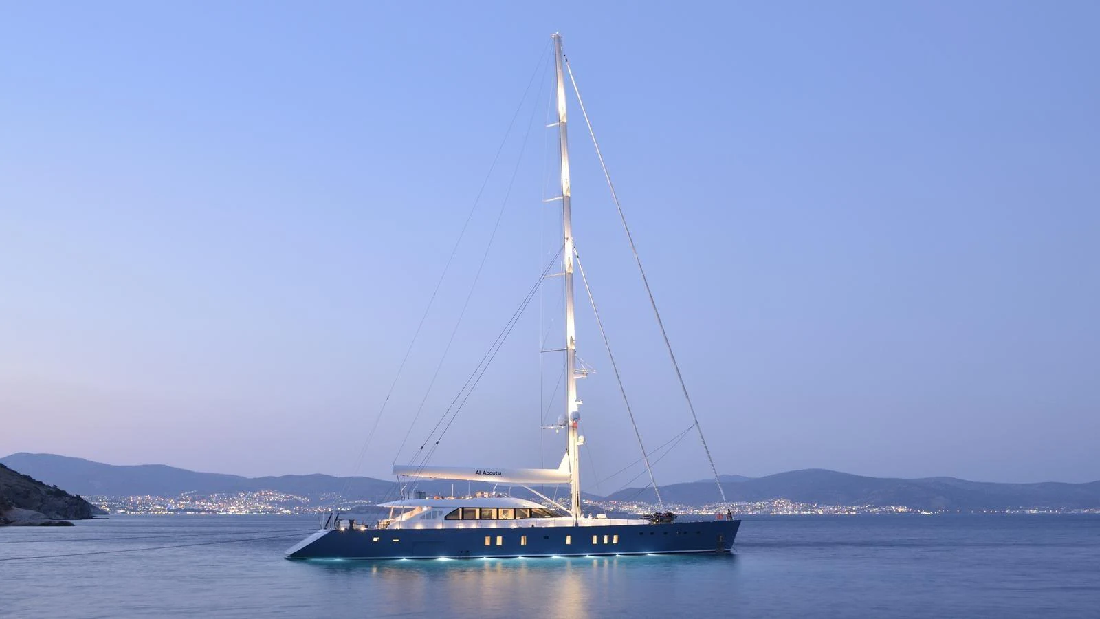 A sleek yacht sails gracefully on calm waters against a twilight backdrop. aboard ALL ABOUT U Yacht for Sale