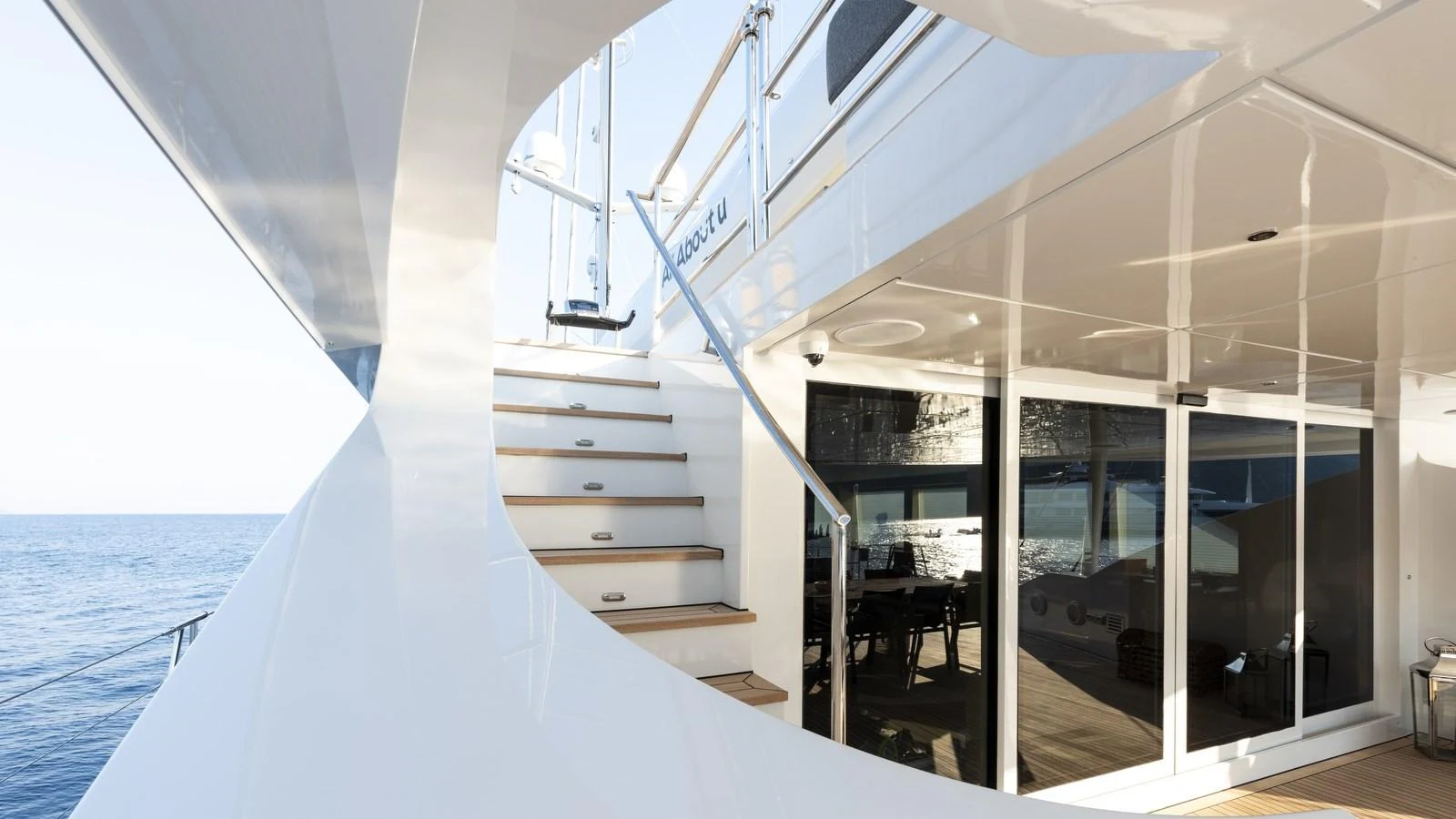 The aft deck features a sleek staircase leading to the upper levels, with a view of the ocean in the background. aboard ALL ABOUT U Yacht for Sale