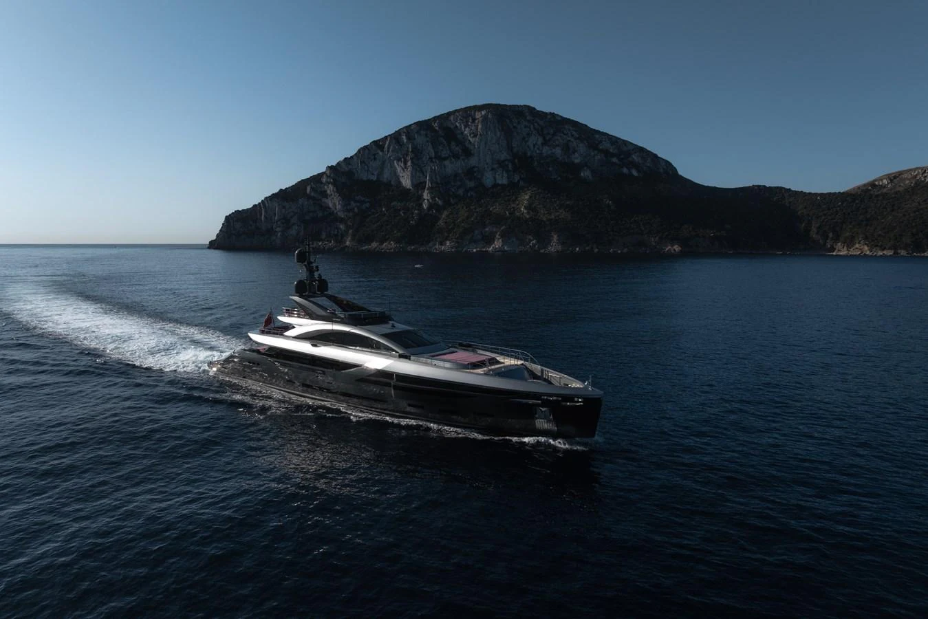 A sleek yacht cruises through calm waters with a scenic mountainous backdrop. aboard FLYING DAGGER III Yacht for Sale