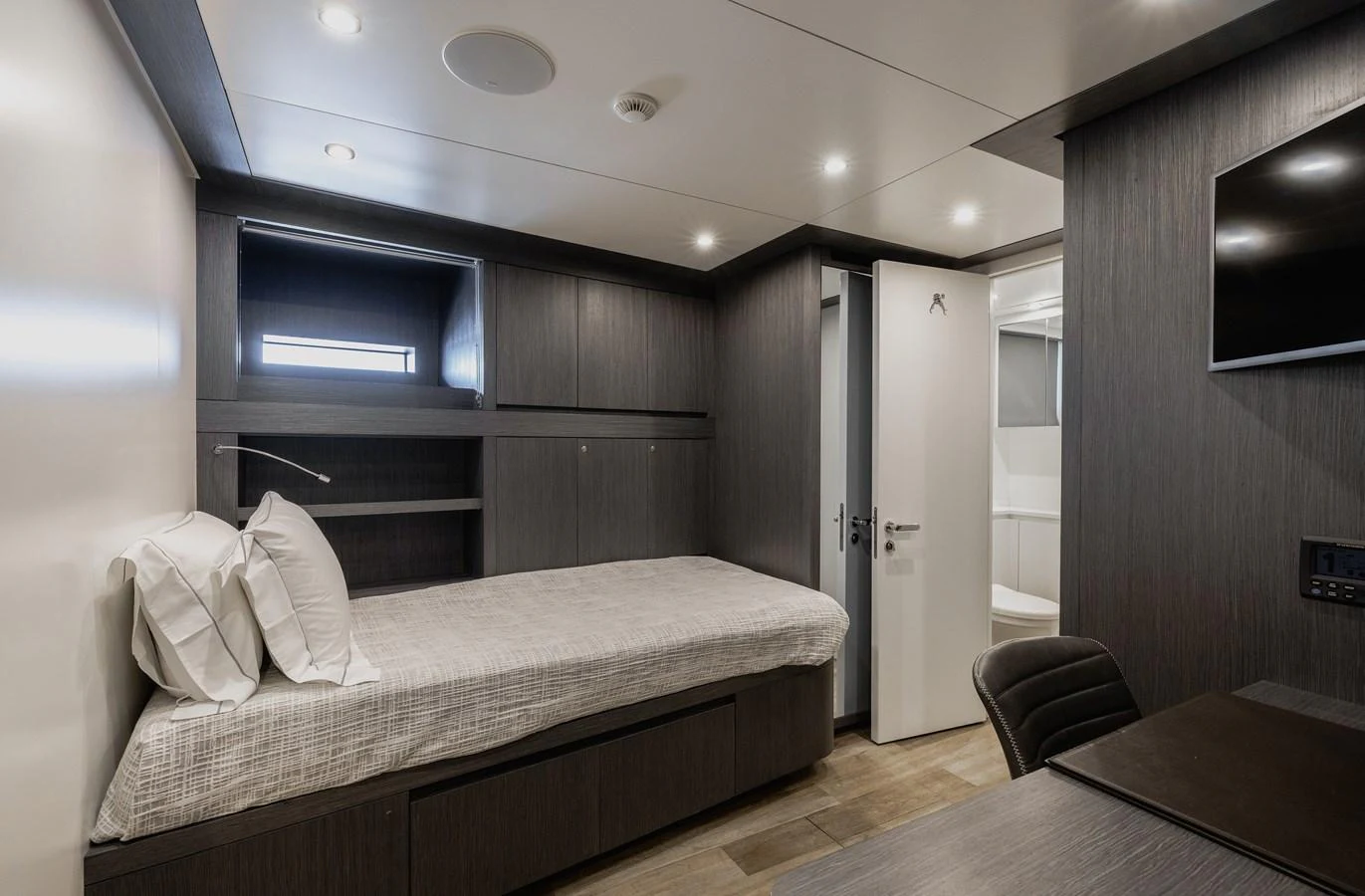 A modern and cozy yacht cabin featuring a single bed, desk, and ample storage space. aboard FLYING DAGGER III Yacht for Sale