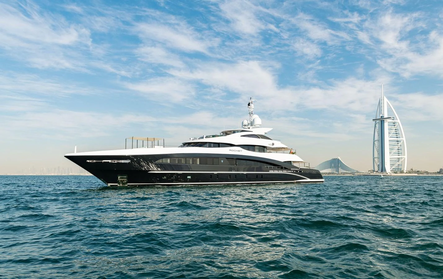 A sleek and modern yacht cruising on calm waters with a cityscape in the background. aboard ROCKET Yacht for Sale