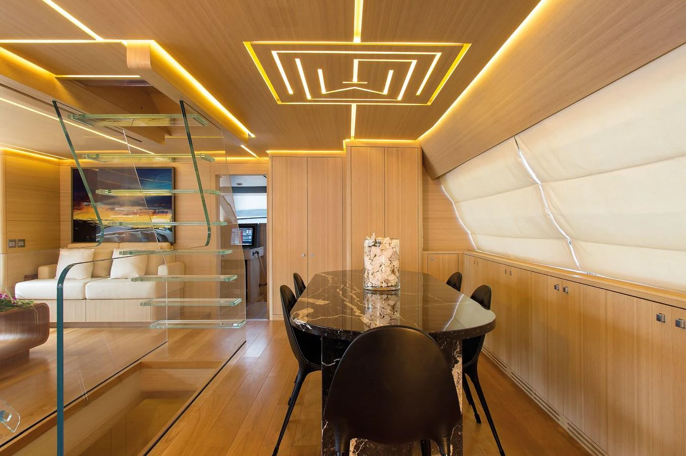 The yacht's dining area features a sleek, modern design with a glass staircase and ambient lighting. aboard OHANA Yacht for Sale