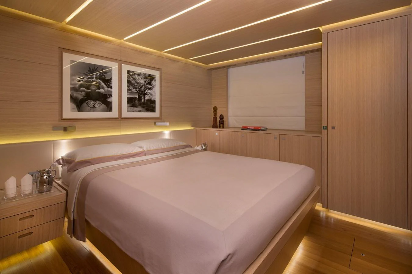 The stateroom features a luxurious bed with elegant wooden finishes and ambient lighting. aboard OHANA Yacht for Sale