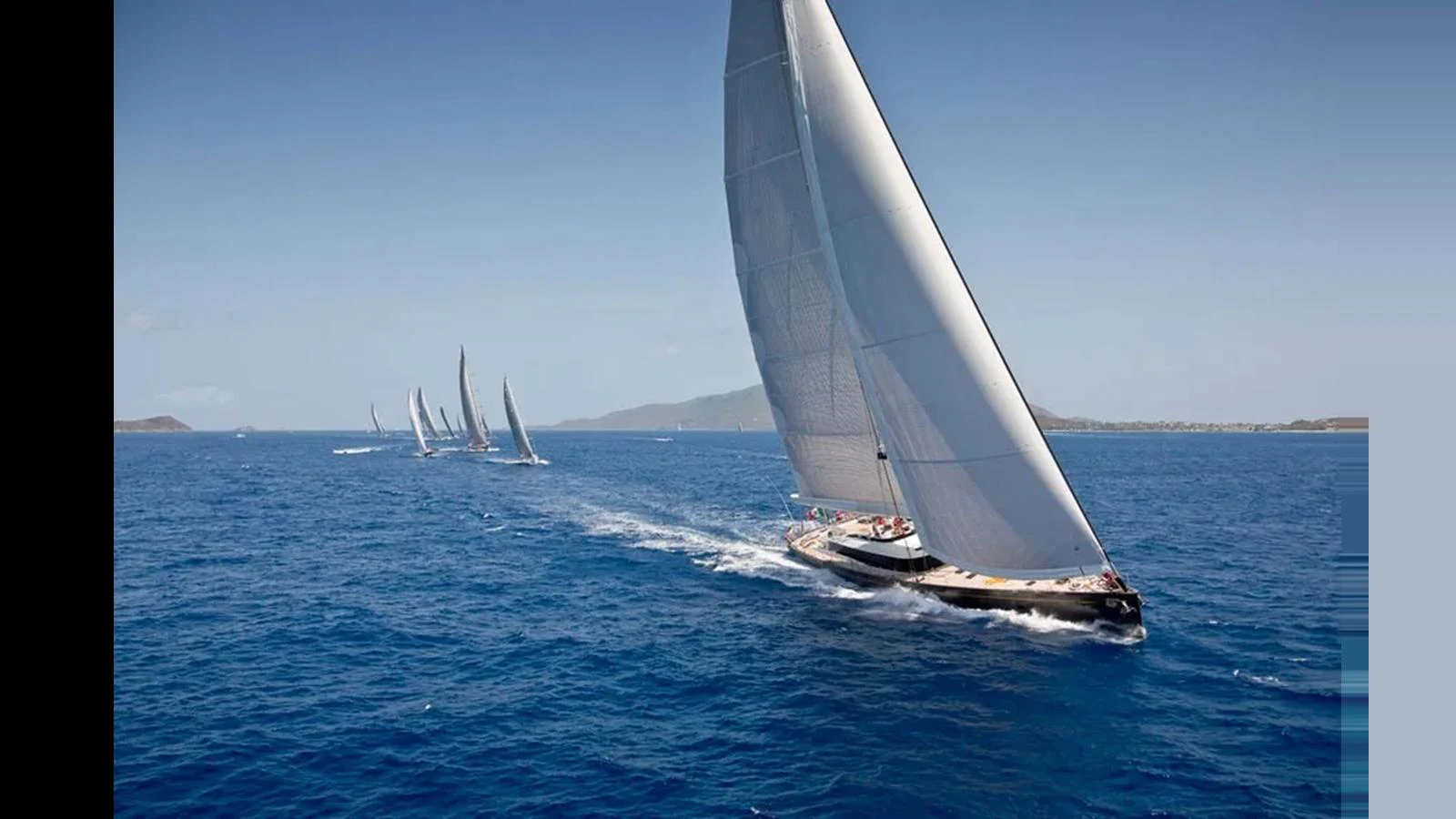 A fleet of sleek sailing yachts glides gracefully across the open sea under clear blue skies. aboard OHANA Yacht for Sale