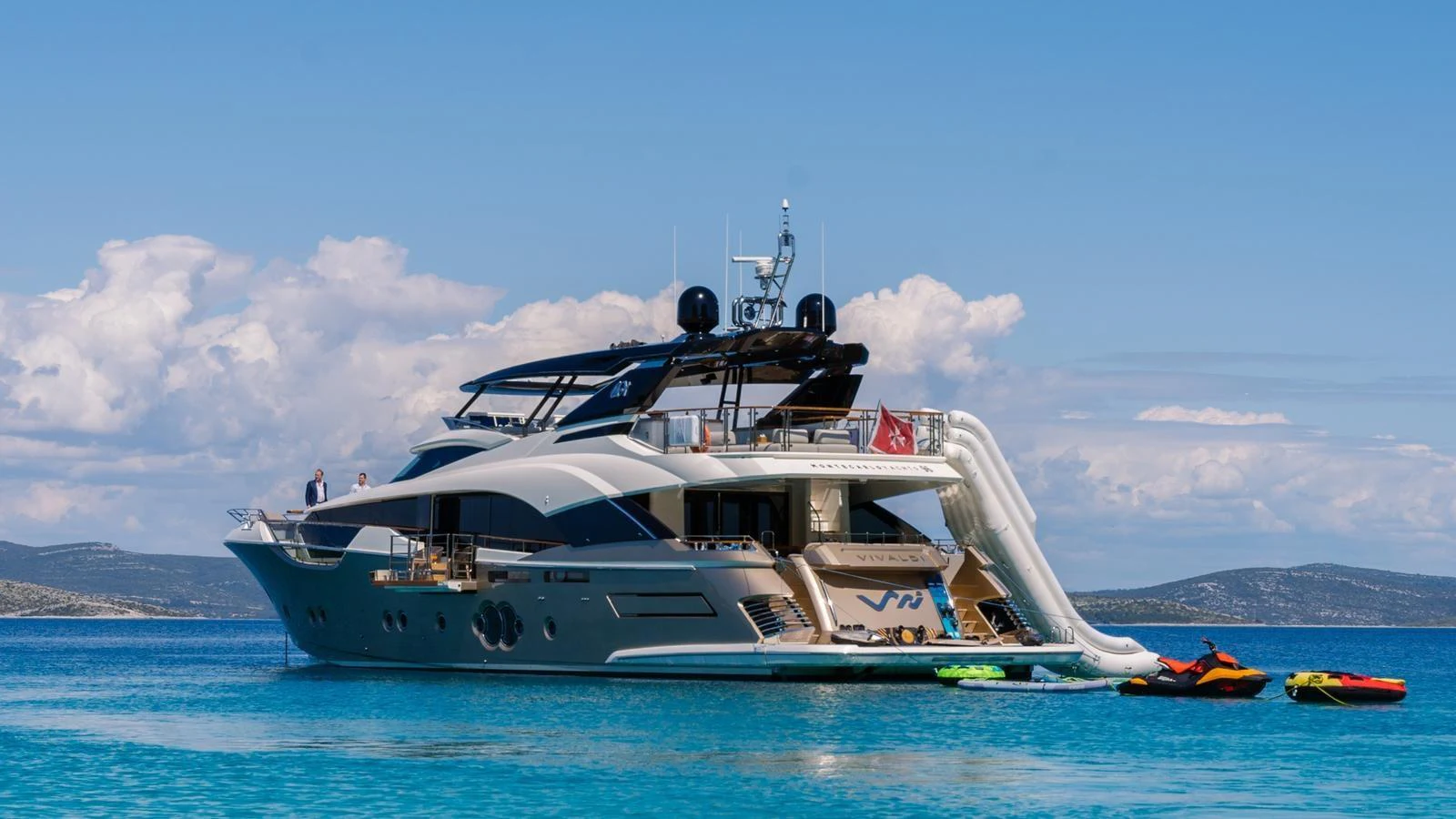 A luxurious yacht anchored in clear blue waters, featuring a slide and water toys for entertainment. aboard VIVALDI Yacht for Sale