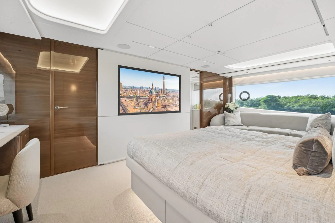 A luxurious stateroom featuring a large bed, a desk, and a wall-mounted TV with scenic views. aboard JUST PERFECT Yacht for Sale
