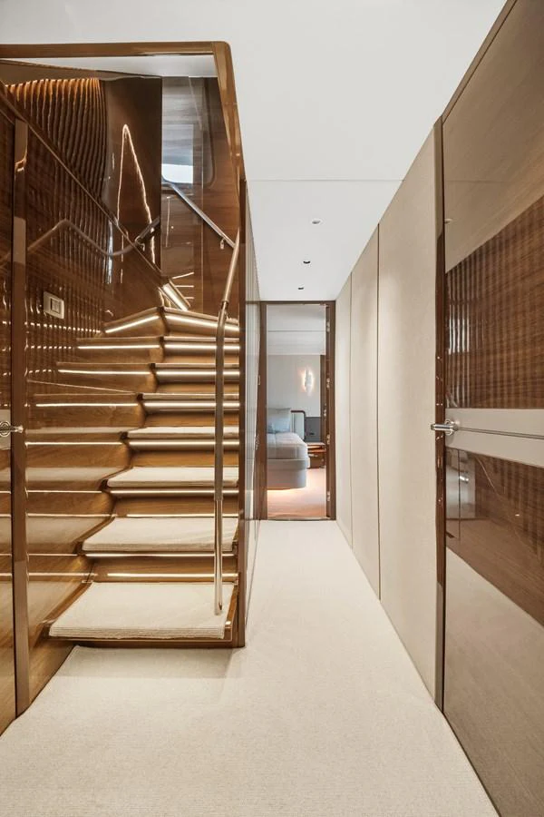 A luxurious interior staircase with wooden finishes and modern lighting leads to the upper deck. aboard JUST PERFECT Yacht for Sale