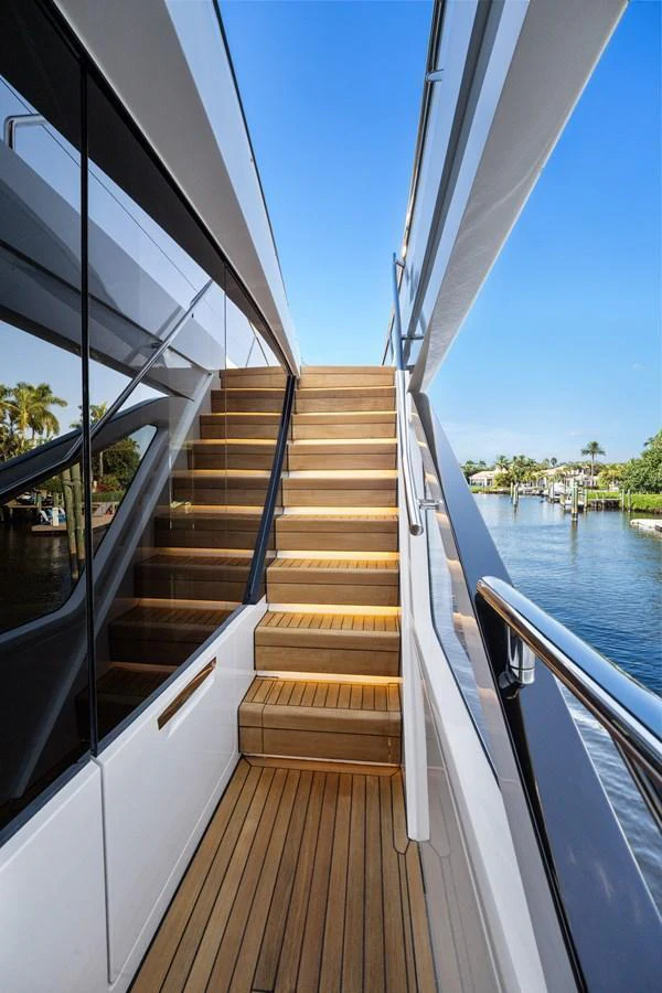 A sleek wooden staircase leads to the upper deck, framed by polished railings and reflective glass panels. aboard JUST PERFECT Yacht for Sale