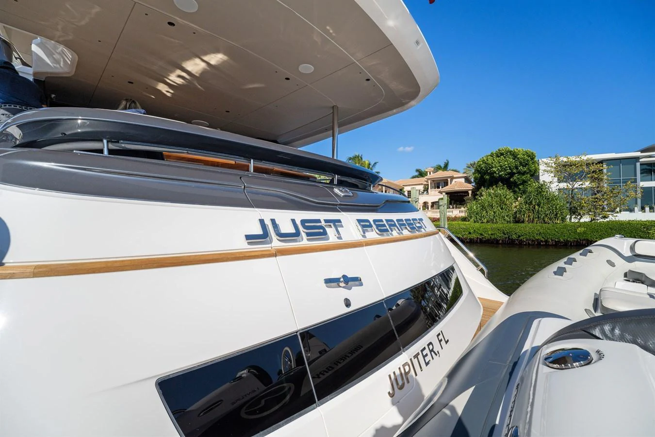 The yacht is docked, showcasing its sleek stern with polished details and a tender nearby. aboard JUST PERFECT Yacht for Sale