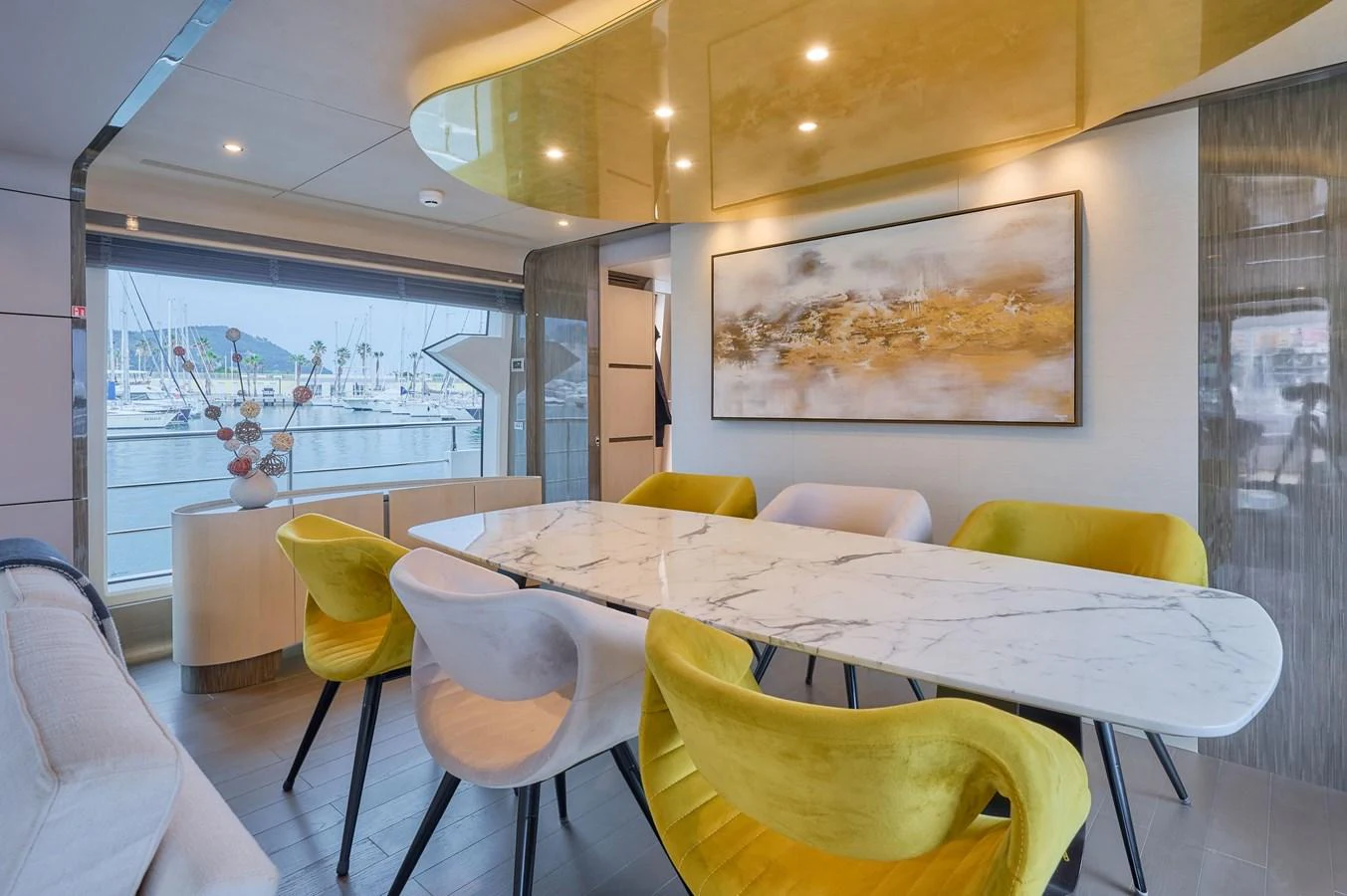 The yacht's dining area features a modern marble table surrounded by stylish chairs, with a large window offering a view of the marina. aboard SUN & SEA Yacht for Sale