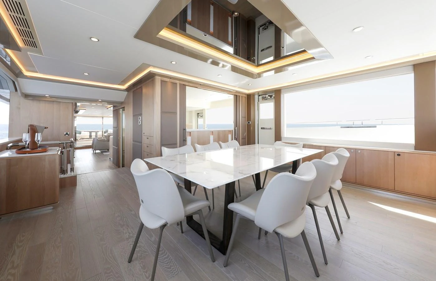 The yacht's dining area features a modern table with sleek white chairs, surrounded by light wood finishes and expansive windows offering stunning sea views. aboard OCEAN ALEXANDER 28L Yacht for Sale