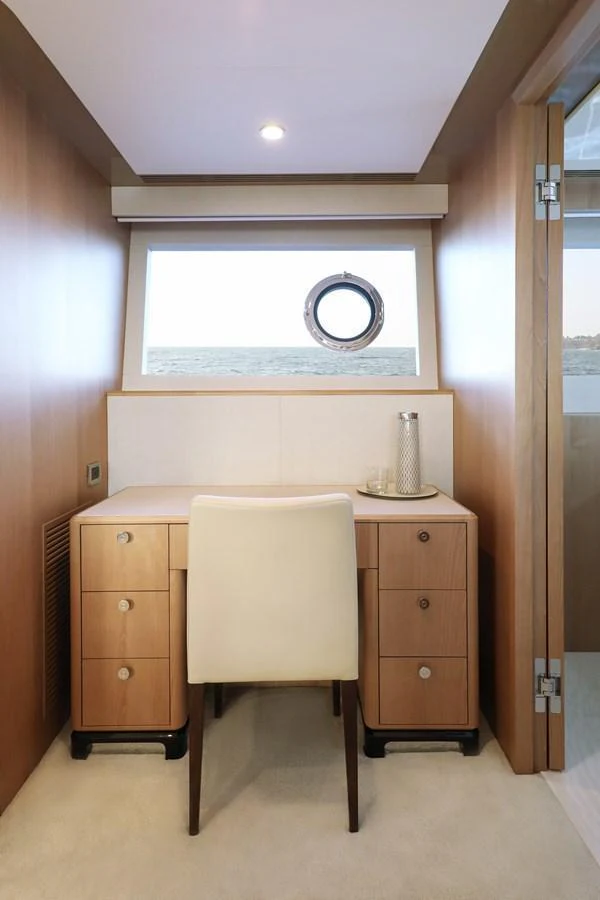 A cozy yacht office with a wooden desk and a comfortable chair, featuring a porthole window with a view of the sea. aboard OCEAN ALEXANDER 28L Yacht for Sale