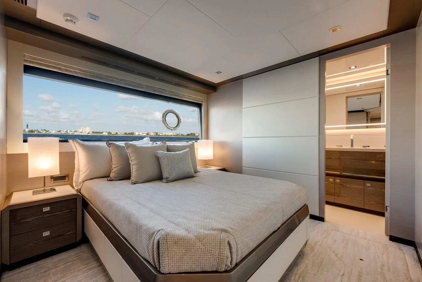 A luxurious stateroom with a large bed, bedside tables, and an ensuite bathroom, featuring a large window with a scenic view. aboard CHAOS Yacht for Sale