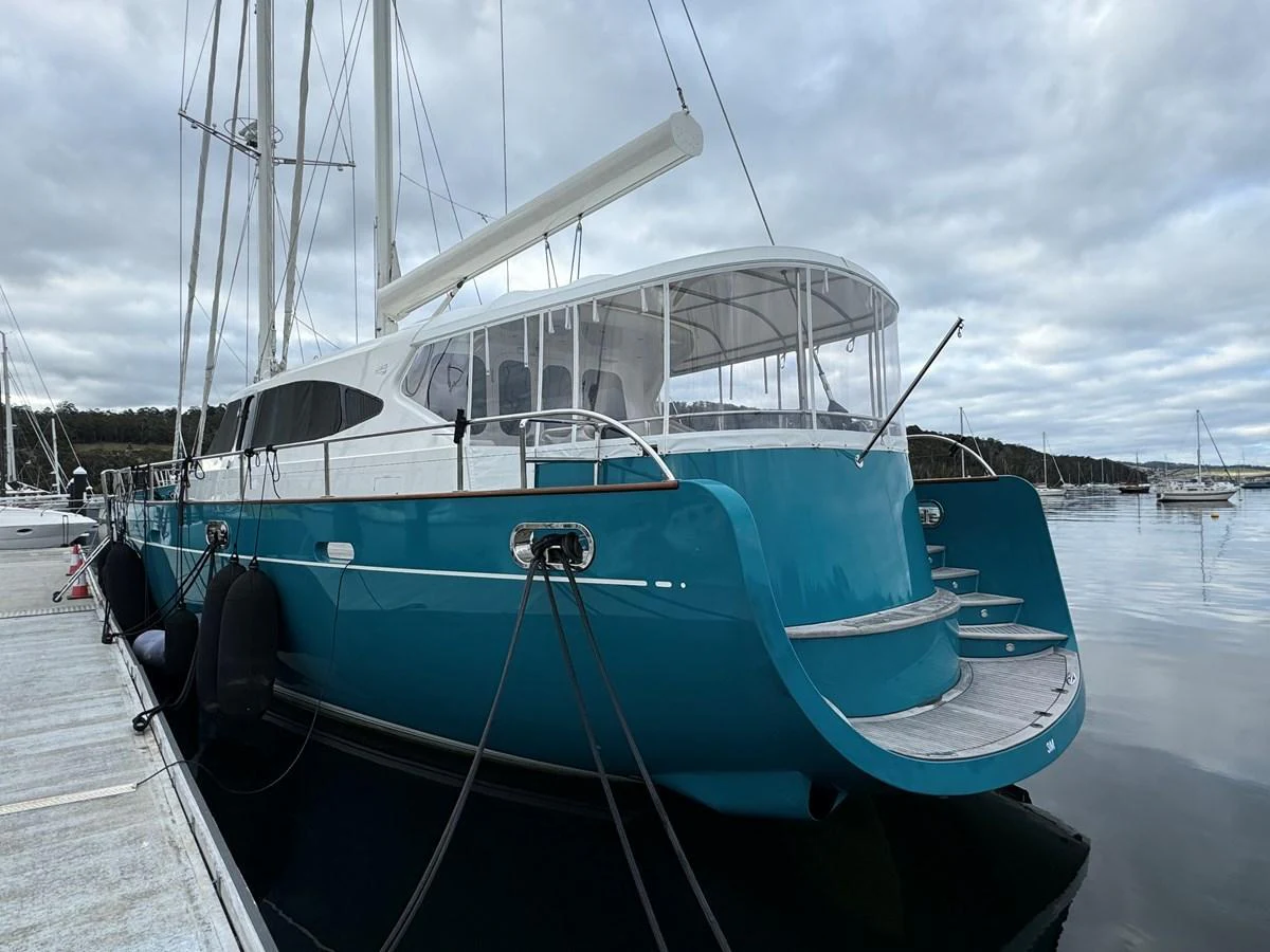 A sleek yacht with a turquoise hull is docked at a marina under a cloudy sky. aboard SV TEAL Yacht for Sale