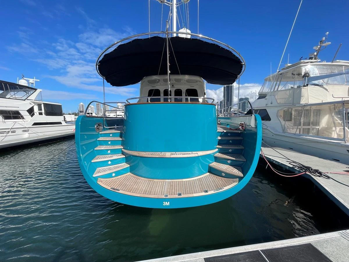 The yacht's vibrant blue stern is docked at a marina, showcasing its elegant design and spacious steps leading to the water. aboard SV TEAL Yacht for Sale