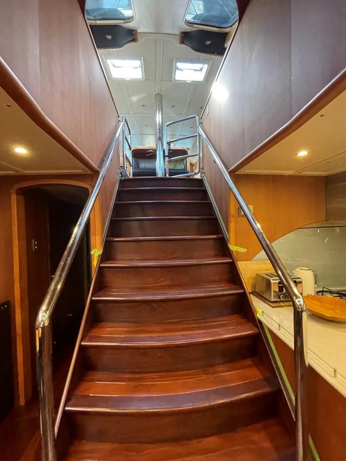 A polished wooden staircase leads to the upper deck, illuminated by natural light from overhead windows. aboard SV TEAL Yacht for Sale