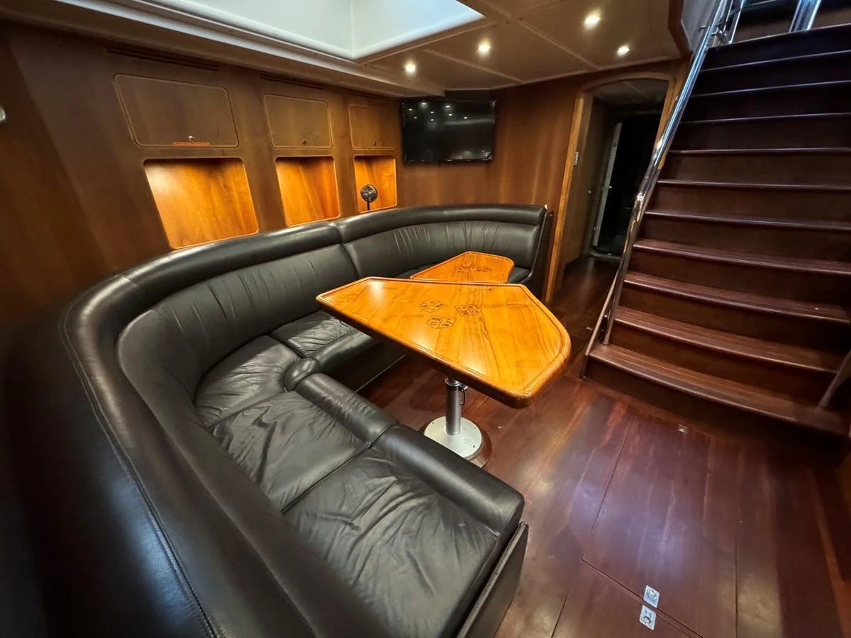 The yacht's saloon features a luxurious curved leather seating area with a wooden table, complemented by rich wood paneling and a staircase leading to the upper deck. aboard SV TEAL Yacht for Sale