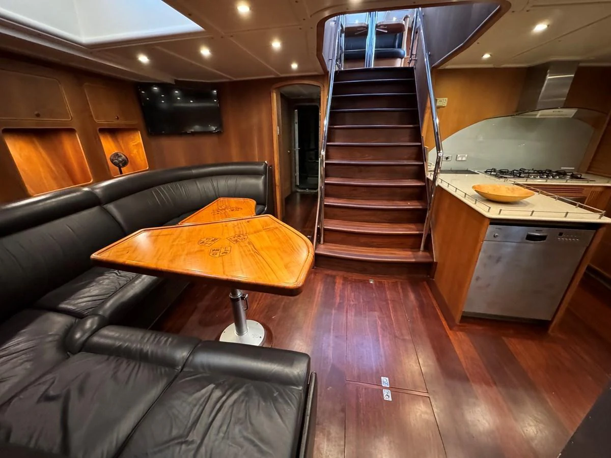 The yacht's salon features a comfortable seating area with a wooden dining table and a staircase leading to the upper deck. aboard SV TEAL Yacht for Sale