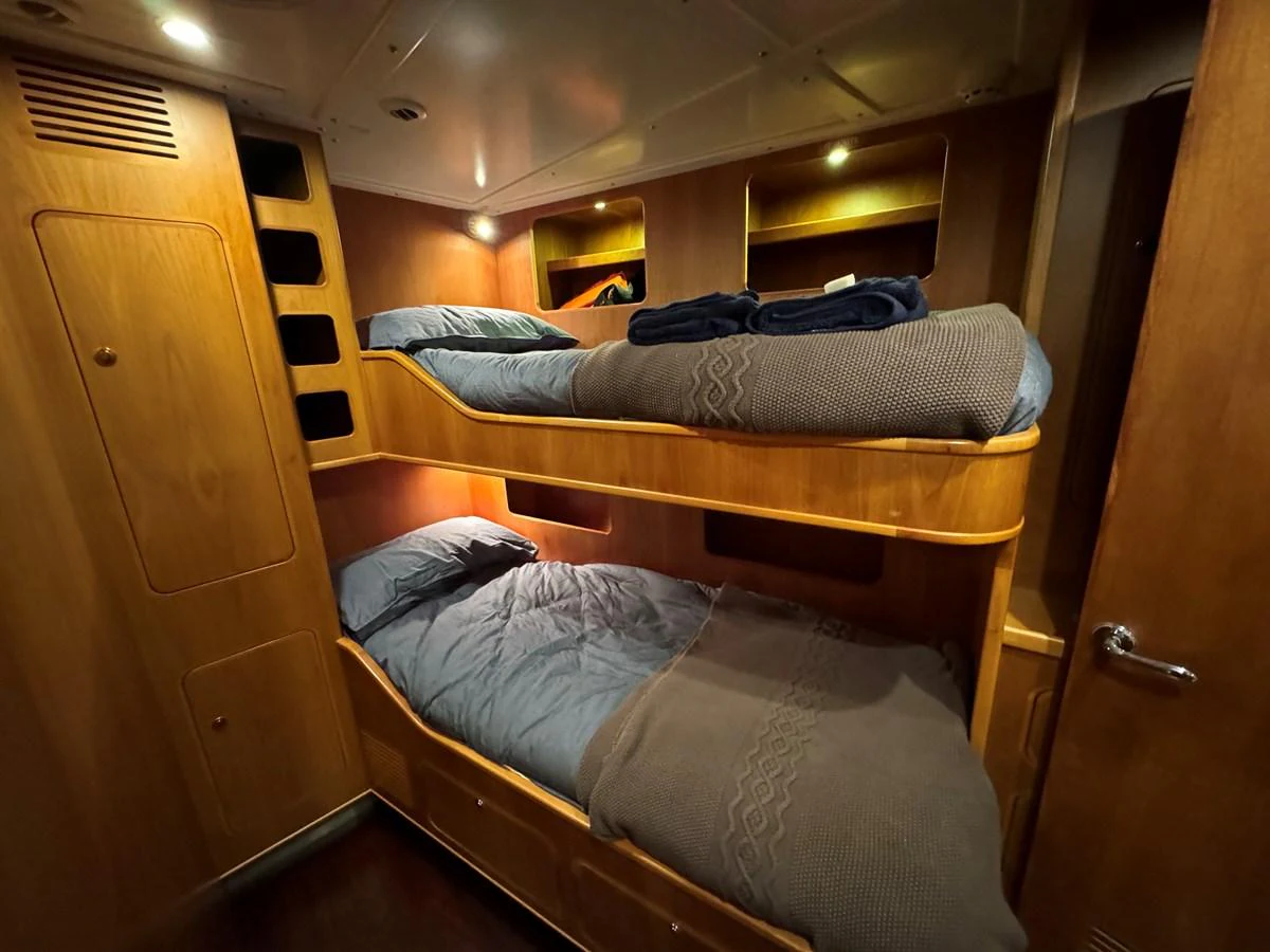 The cozy bunk room features wooden paneling and comfortable bedding, creating a warm and inviting atmosphere. aboard SV TEAL Yacht for Sale