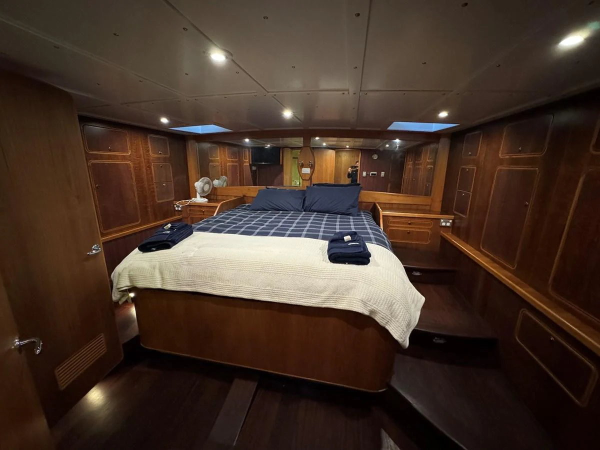 The master stateroom features a spacious bed with elegant wood paneling and ambient lighting. aboard SV TEAL Yacht for Sale