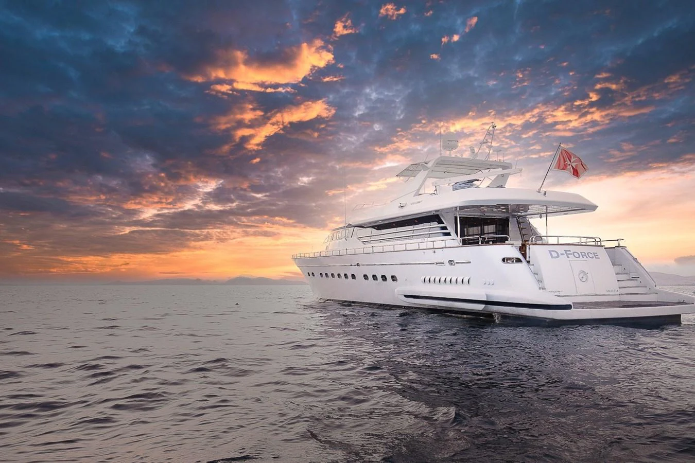 A luxurious yacht is anchored on calm waters under a dramatic sunset sky. aboard D-FORCE Yacht for Sale