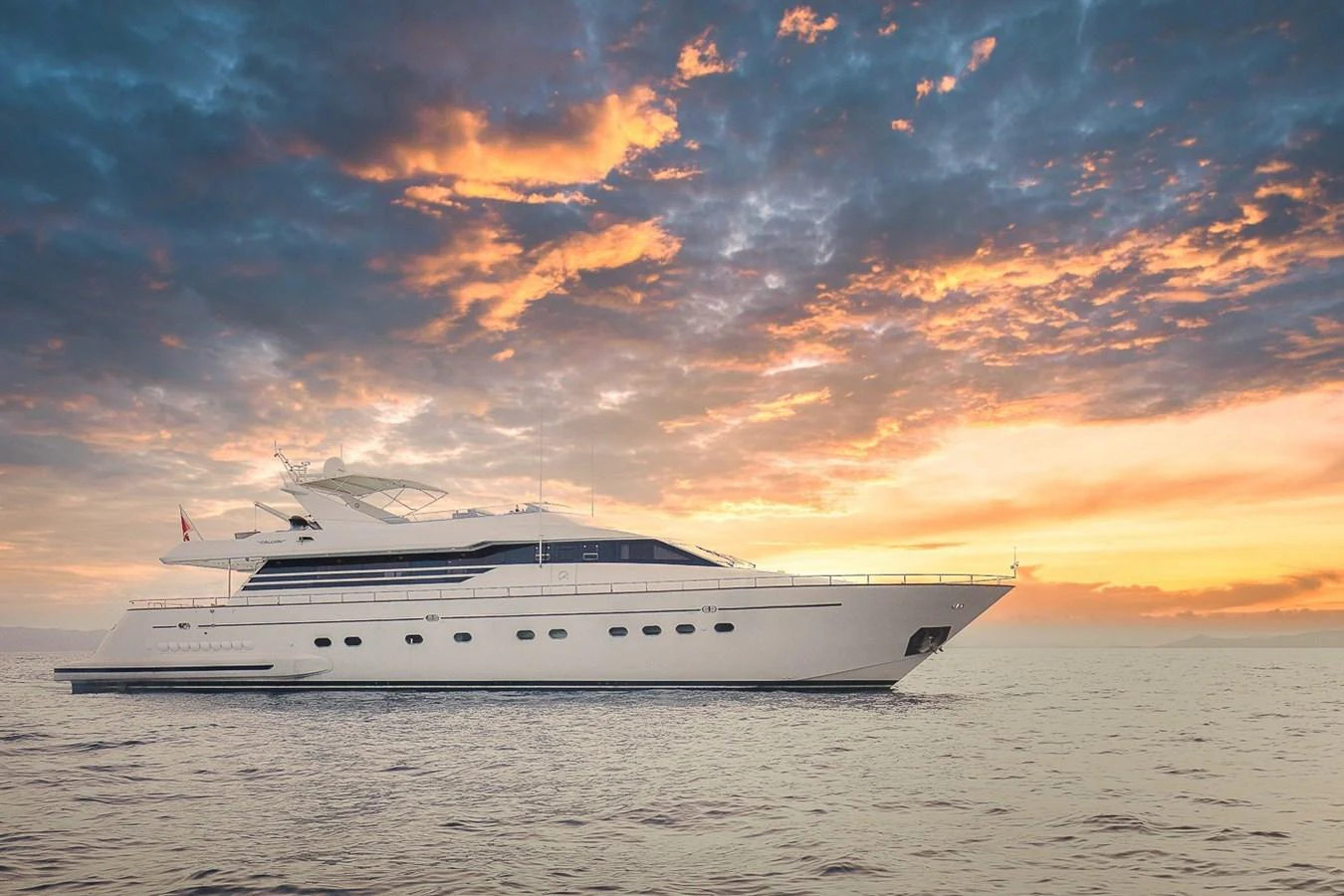A sleek yacht glides gracefully on calm waters against a stunning sunset backdrop. aboard D-FORCE Yacht for Sale