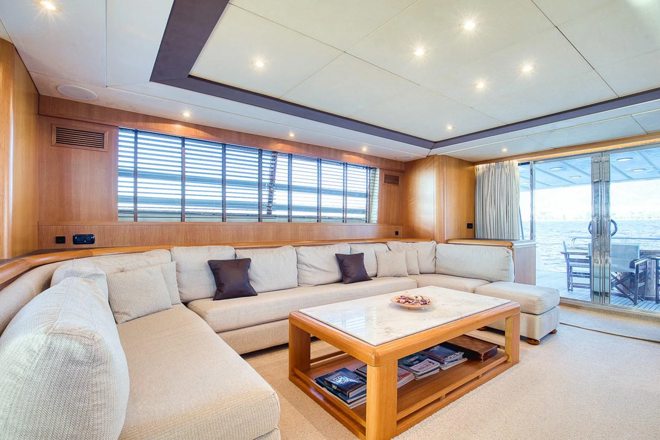 The spacious salon features a large, comfortable sectional sofa and a wooden coffee table, with ample natural light streaming in through the windows. aboard D-FORCE Yacht for Sale