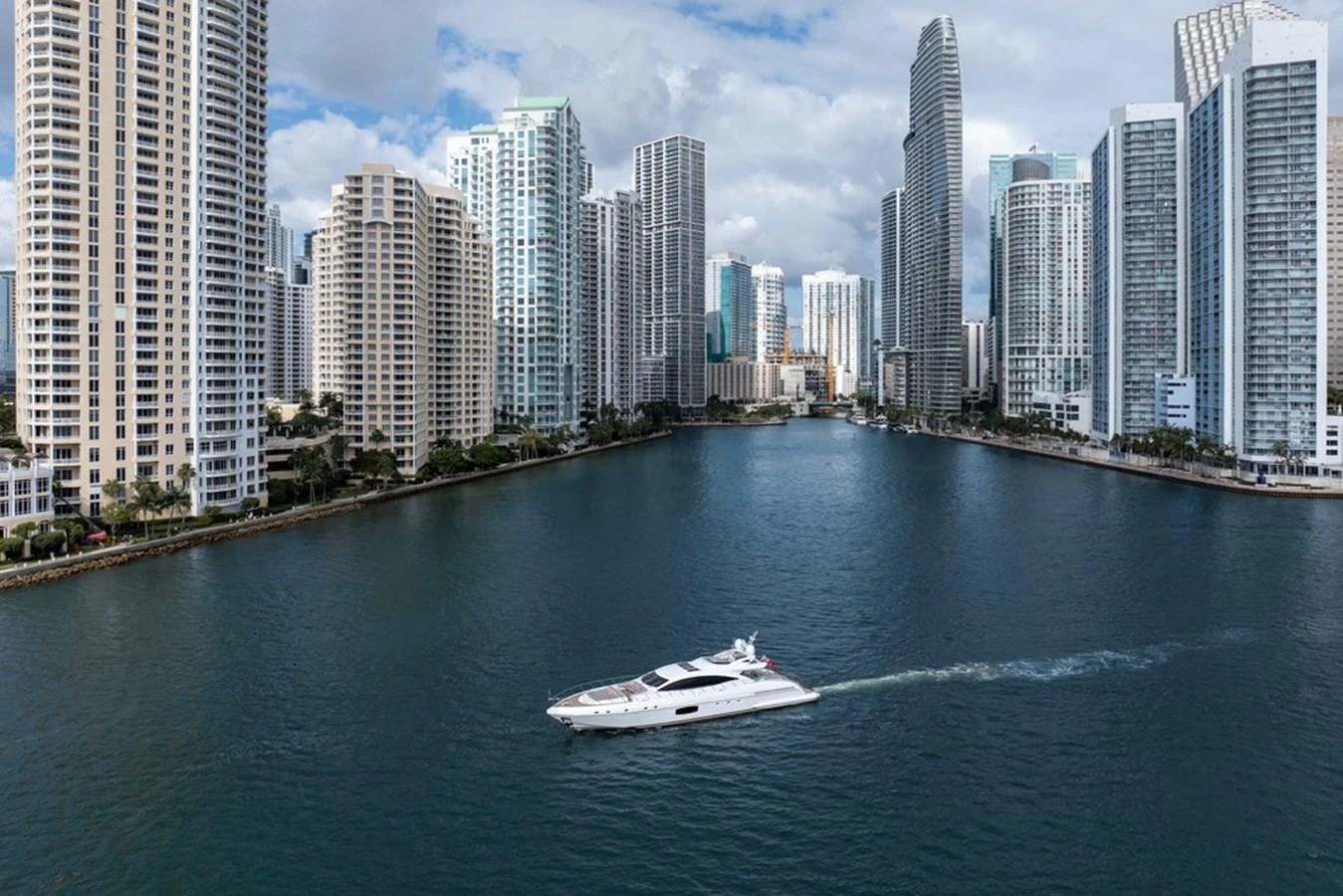 A sleek yacht cruises through a cityscape waterway surrounded by towering buildings. aboard SAYONARA Yacht for Sale