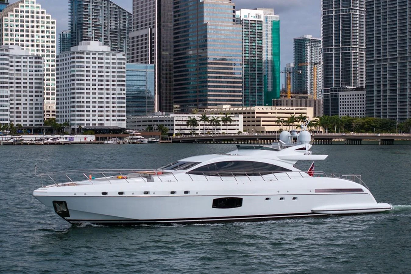 A sleek white yacht cruises past a city skyline, showcasing its modern design and luxurious appeal. aboard SAYONARA Yacht for Sale